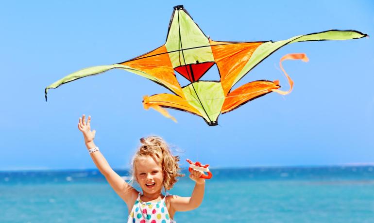 Bambina felice con aquilone colorato sulla spiaggia.