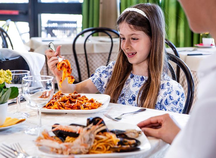 Mädchen isst freudig Pasta im Restaurant.