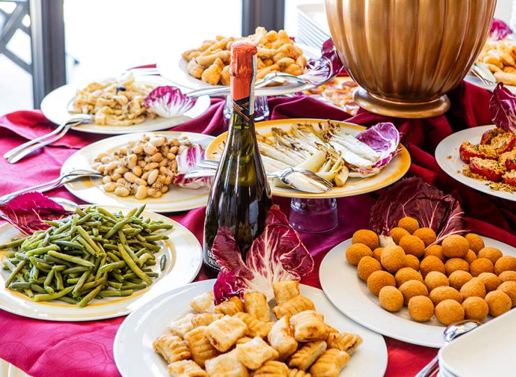 Buffet mit Gemüse, Snacks und Wein auf rotem Tischtuch.