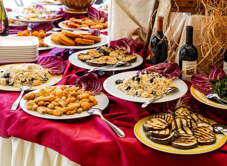 Buffet mit Gerichten und Wein auf roter Tischdecke.