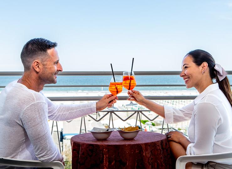 Paar stößt mit Cocktails auf einer Terrasse am Meer an.